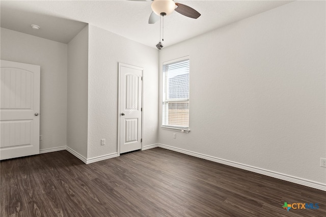 empty room featuring ceiling fan, baseboards, and dark wood finished floors