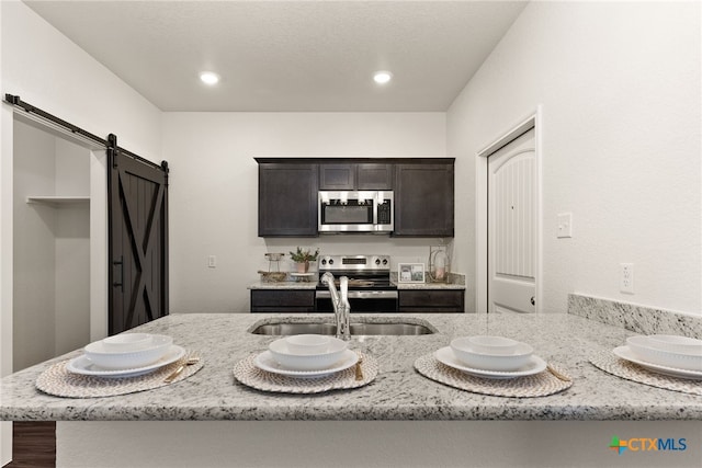 kitchen with a sink, light stone counters, recessed lighting, a barn door, and appliances with stainless steel finishes