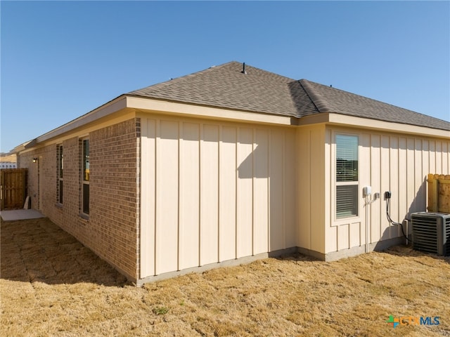 view of side of home featuring brick siding, board and batten siding, a shingled roof, fence, and cooling unit