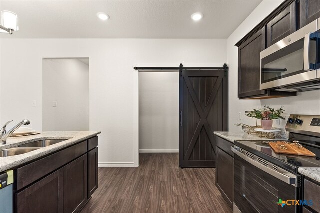 kitchen with a sink, dark brown cabinetry, dark wood-type flooring, appliances with stainless steel finishes, and a barn door