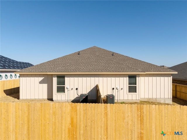 rear view of house featuring board and batten siding, a shingled roof, and fence