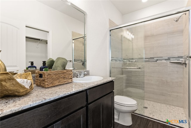 bathroom with wood finished floors, toilet, a stall shower, and vanity