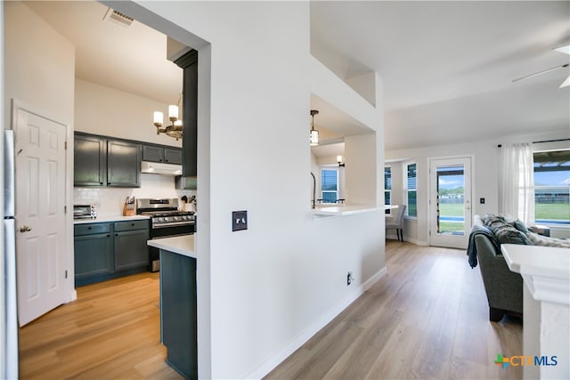 kitchen with decorative backsplash, ceiling fan with notable chandelier, decorative light fixtures, light hardwood / wood-style flooring, and stainless steel range with gas stovetop