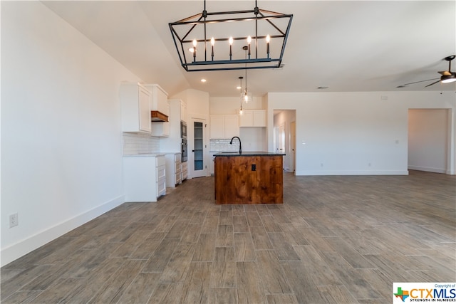 kitchen with a center island with sink, tasteful backsplash, dark hardwood / wood-style floors, white cabinets, and pendant lighting