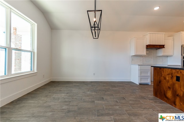 kitchen featuring white cabinets, decorative light fixtures, vaulted ceiling, and backsplash