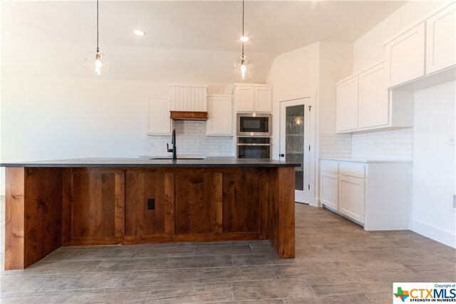 kitchen with white cabinets, decorative light fixtures, an island with sink, and stainless steel appliances