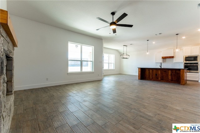 unfurnished living room with hardwood / wood-style floors, ceiling fan, a stone fireplace, and sink