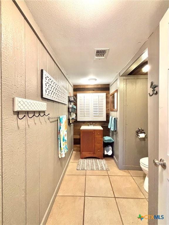 bathroom with toilet, wood walls, tile patterned flooring, a textured ceiling, and vanity