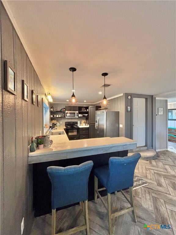 kitchen with kitchen peninsula, wooden walls, light parquet floors, a kitchen breakfast bar, and stainless steel appliances