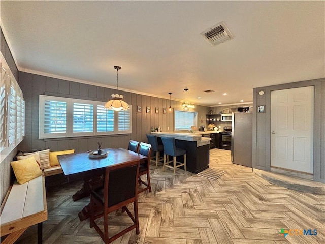 dining area with light parquet flooring, wood walls, sink, and crown molding