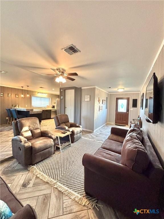 living room featuring ceiling fan, wooden walls, and ornamental molding