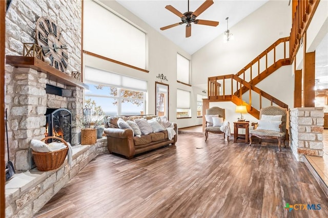 living room with ceiling fan, a stone fireplace, wood-type flooring, and high vaulted ceiling