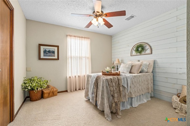 carpeted bedroom with ceiling fan, wooden walls, and a textured ceiling