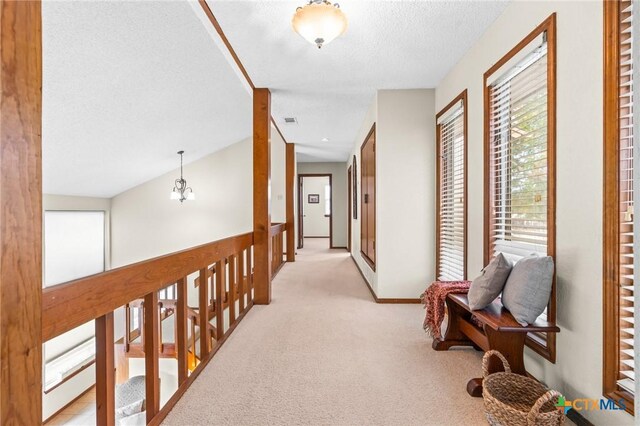 corridor with light colored carpet, a textured ceiling, and vaulted ceiling