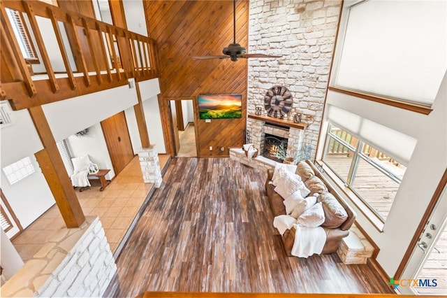 living room featuring ceiling fan, light hardwood / wood-style flooring, high vaulted ceiling, wood walls, and a fireplace