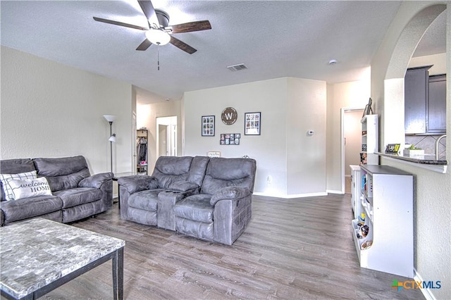 living room with dark hardwood / wood-style flooring, ceiling fan, and a textured ceiling