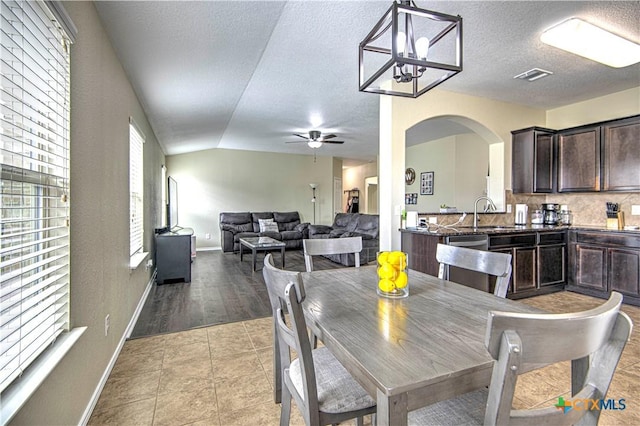 dining space with vaulted ceiling, ceiling fan with notable chandelier, sink, light tile patterned floors, and a textured ceiling