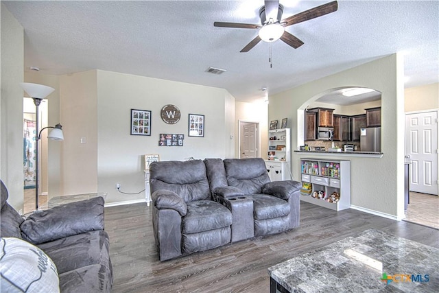 living room featuring dark wood-type flooring, ceiling fan, and a textured ceiling