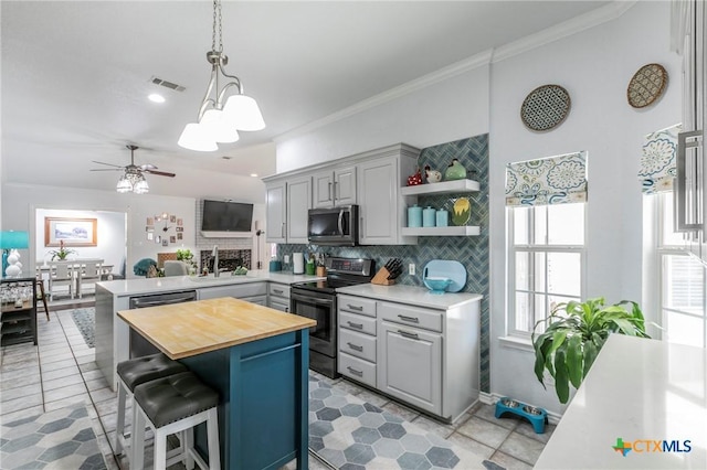 kitchen with kitchen peninsula, a breakfast bar, decorative light fixtures, wood counters, and appliances with stainless steel finishes