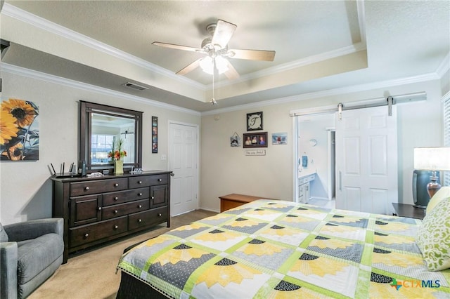 bedroom with a tray ceiling, a barn door, crown molding, and light carpet