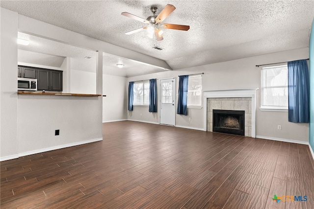 unfurnished living room with a textured ceiling, vaulted ceiling, ceiling fan, and a tiled fireplace