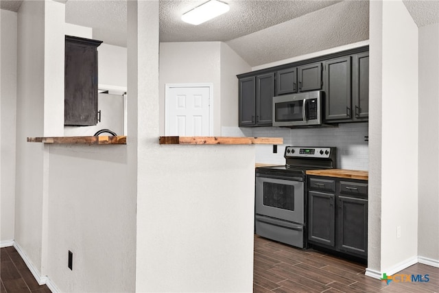 kitchen with decorative backsplash, appliances with stainless steel finishes, kitchen peninsula, butcher block counters, and lofted ceiling