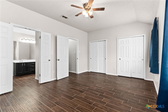 unfurnished bedroom with lofted ceiling, two closets, ceiling fan, a textured ceiling, and connected bathroom