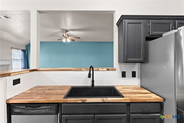 kitchen with butcher block counters, sink, tasteful backsplash, a textured ceiling, and appliances with stainless steel finishes