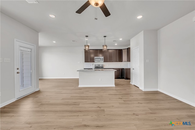 kitchen with dark brown cabinetry, hanging light fixtures, light hardwood / wood-style flooring, a kitchen island with sink, and appliances with stainless steel finishes