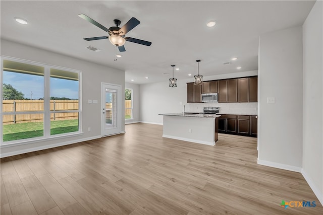 kitchen with a kitchen island with sink, stainless steel appliances, dark brown cabinetry, hanging light fixtures, and light hardwood / wood-style flooring