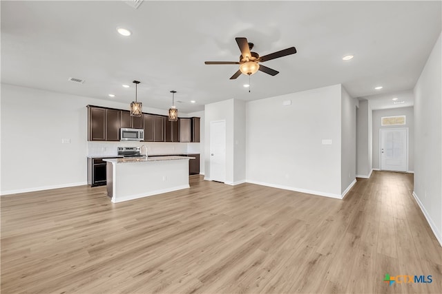 kitchen with stainless steel appliances, dark brown cabinetry, hanging light fixtures, an island with sink, and light hardwood / wood-style flooring