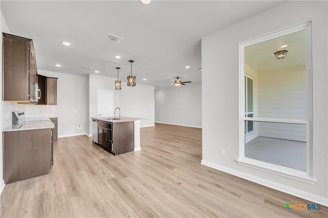 kitchen with sink, ceiling fan, decorative light fixtures, a kitchen island with sink, and light wood-type flooring