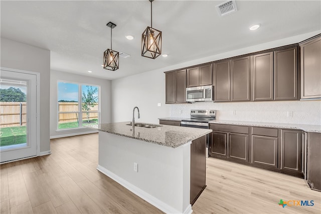 kitchen featuring light hardwood / wood-style floors, stainless steel appliances, light stone counters, hanging light fixtures, and sink