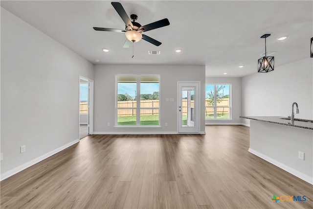 unfurnished living room featuring plenty of natural light, sink, ceiling fan, and light hardwood / wood-style flooring