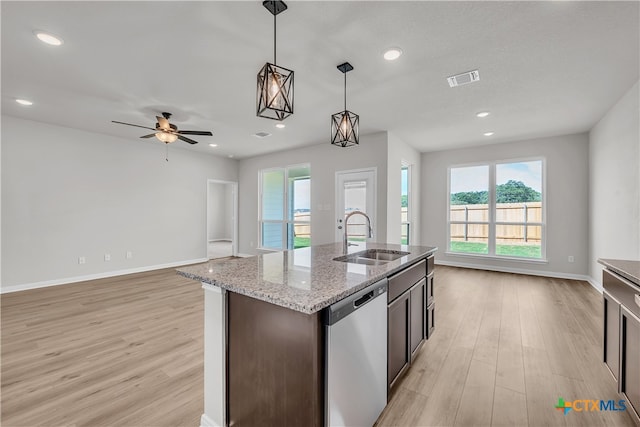 kitchen with hanging light fixtures, sink, stainless steel dishwasher, light stone countertops, and light wood-type flooring