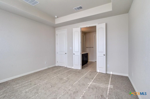 unfurnished bedroom featuring light colored carpet and a raised ceiling