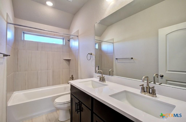 full bathroom with tiled shower / bath, vaulted ceiling, vanity, and toilet