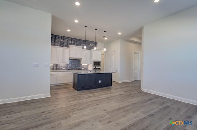 kitchen with built in microwave, white cabinetry, light hardwood / wood-style floors, decorative light fixtures, and a center island with sink