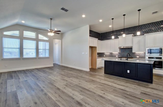 kitchen featuring white cabinetry, an island with sink, light hardwood / wood-style floors, vaulted ceiling, and appliances with stainless steel finishes