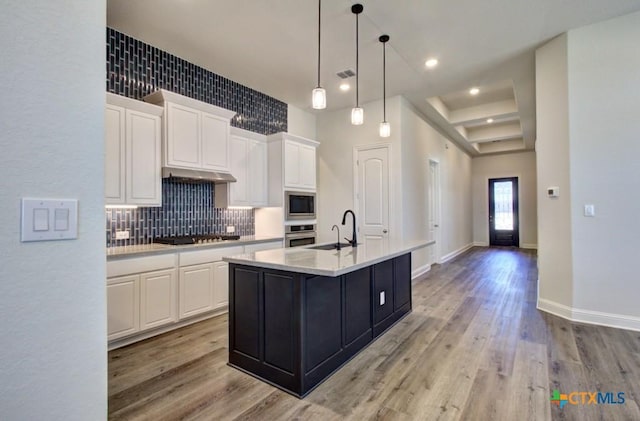 kitchen with gas stovetop, built in microwave, a center island with sink, white cabinets, and oven