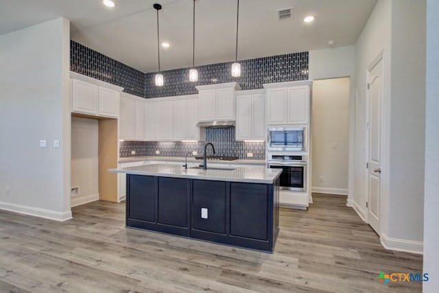 kitchen featuring built in microwave, stainless steel oven, white cabinets, and a kitchen island with sink