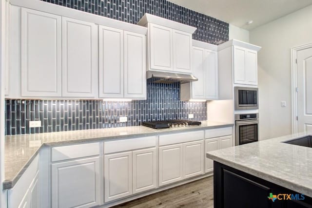 kitchen featuring white cabinets, light hardwood / wood-style flooring, decorative backsplash, light stone counters, and stainless steel appliances