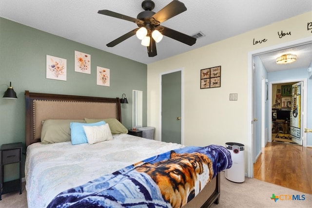 carpeted bedroom featuring ceiling fan, visible vents, and a textured ceiling