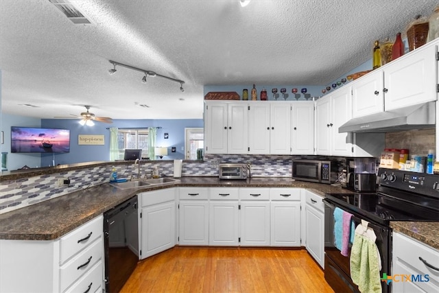 kitchen featuring visible vents, a peninsula, under cabinet range hood, black appliances, and a sink