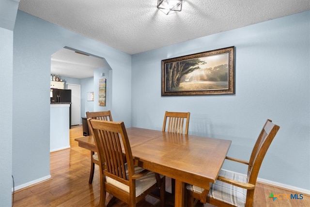 dining room with arched walkways, light wood finished floors, a textured ceiling, and baseboards