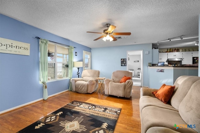 living area featuring a ceiling fan, a textured ceiling, baseboards, and wood finished floors