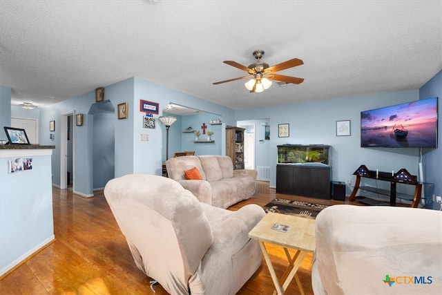 living area featuring ceiling fan, a textured ceiling, baseboards, and wood finished floors