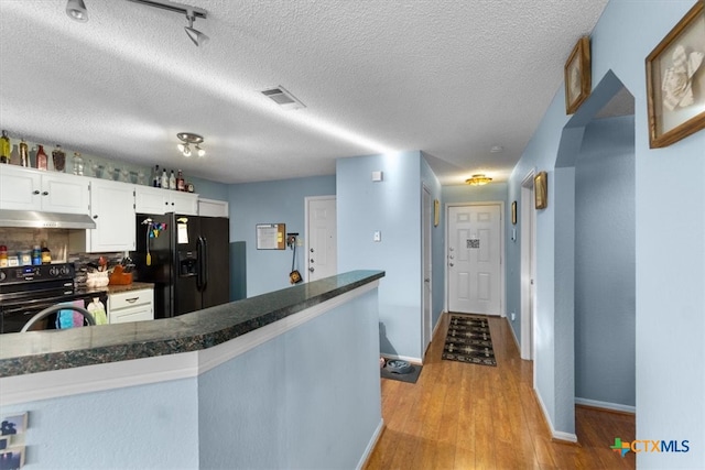 kitchen with dark countertops, light wood-style flooring, white cabinets, under cabinet range hood, and black appliances