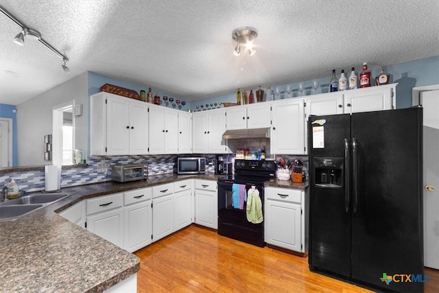 kitchen with dark countertops, white cabinetry, light wood-type flooring, under cabinet range hood, and black appliances