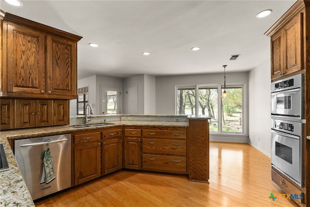 kitchen featuring light stone counters, appliances with stainless steel finishes, sink, light hardwood / wood-style floors, and kitchen peninsula